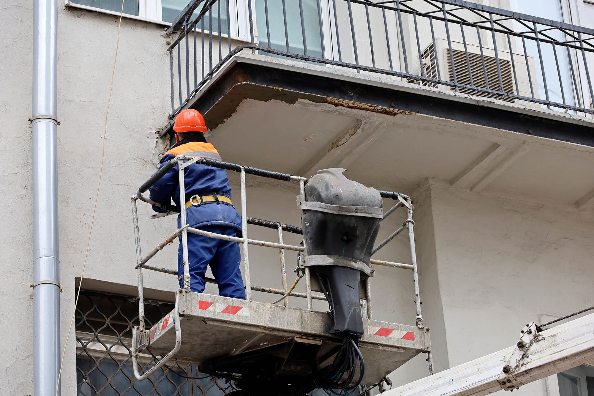Worker in hydraulic lifting ramp repair the balcony. Builder on lifting platform standing near the building wall, construction and repair works